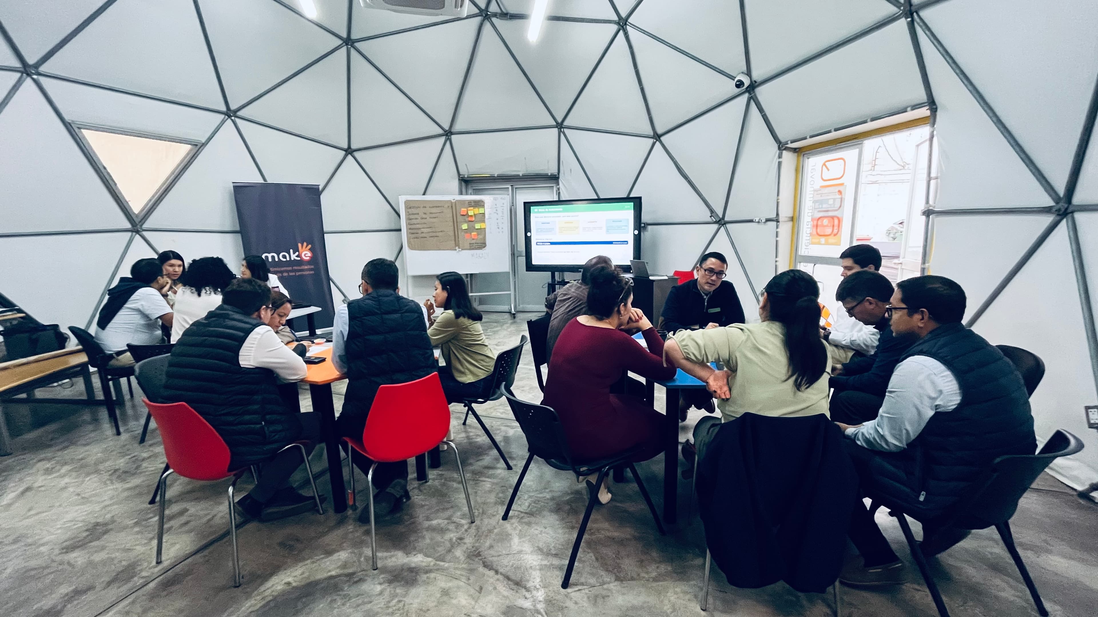 Grupo de personas participando en un taller colaborativo dentro de un domo geodésico blanco.