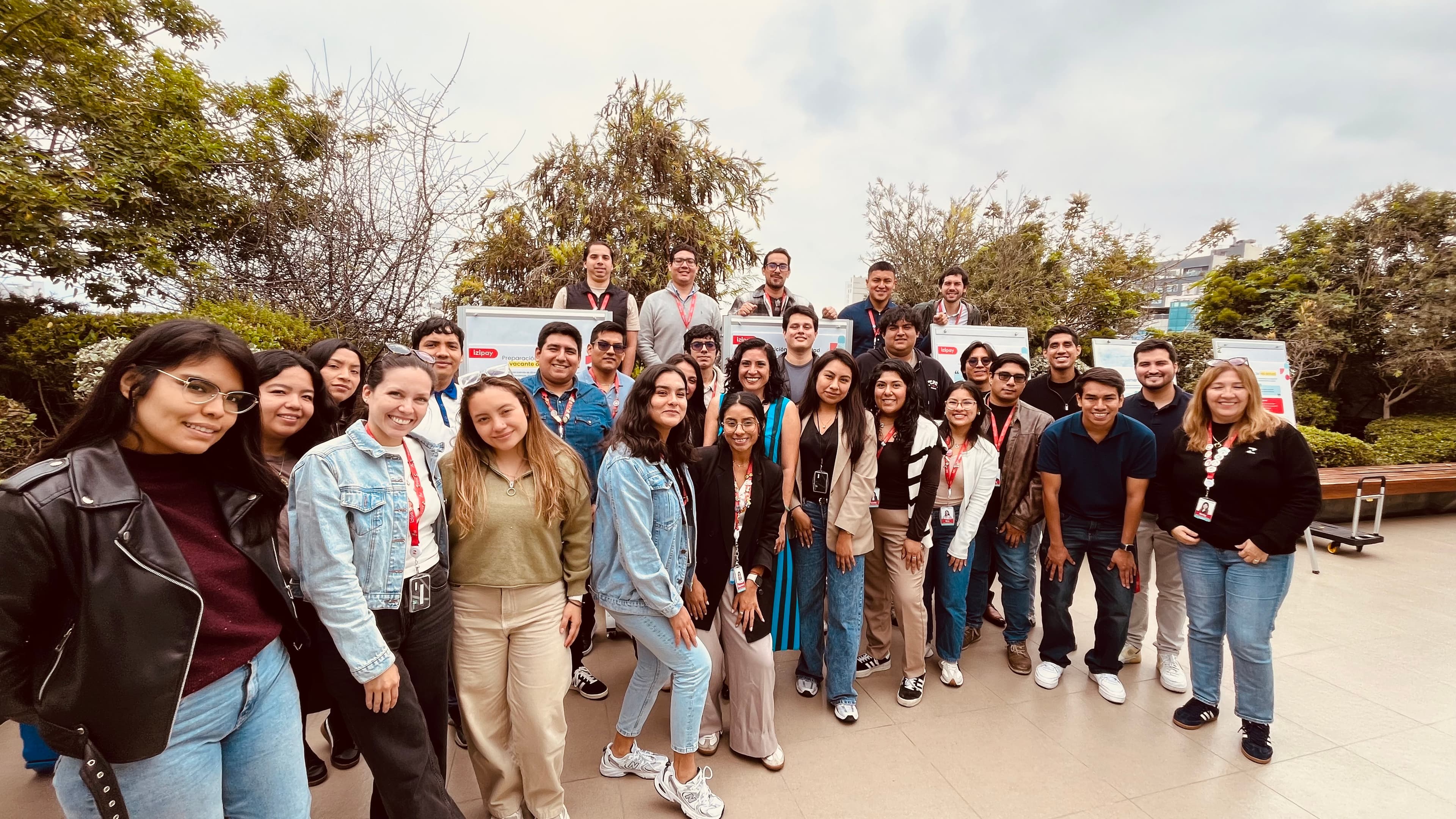 Grupo de jóvenes profesionales sonriendo y posando en una terraza exterior con vegetación.