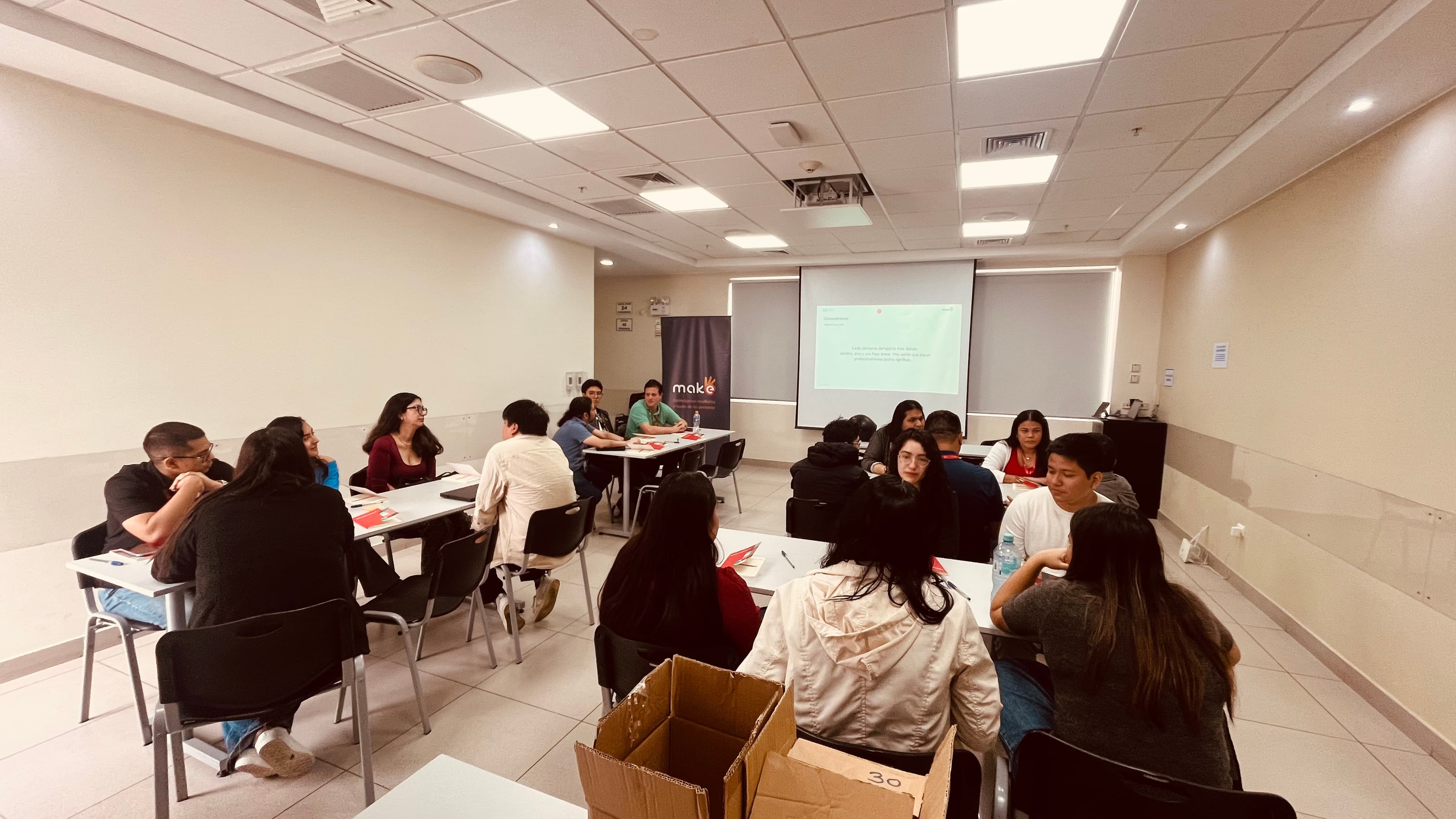 Grupo de personas sentadas en mesas durante un taller educativo en un aula iluminada.
