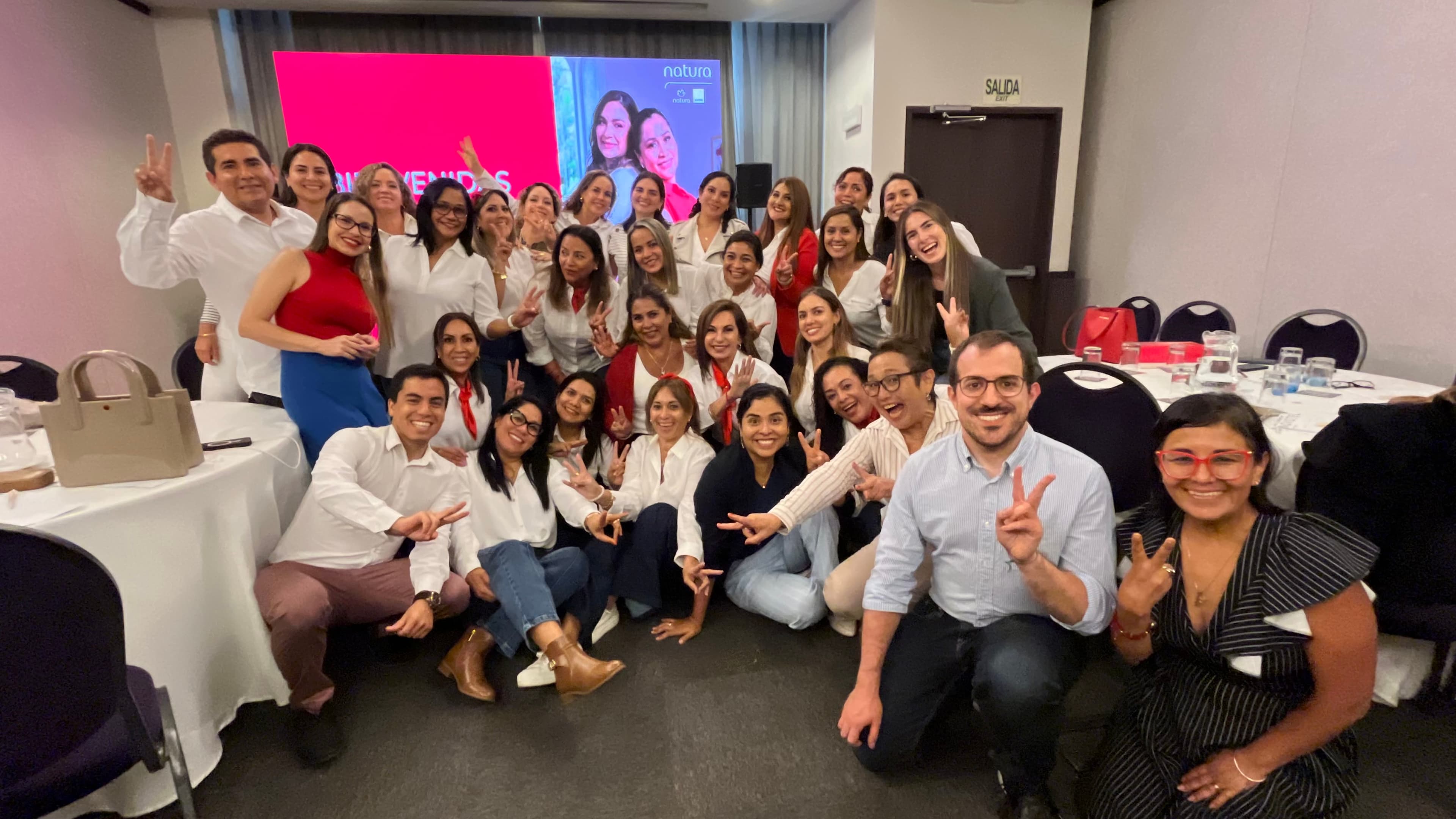 Grupo numeroso de personas sonrientes posando juntas en un evento corporativo con vestimenta blanca.