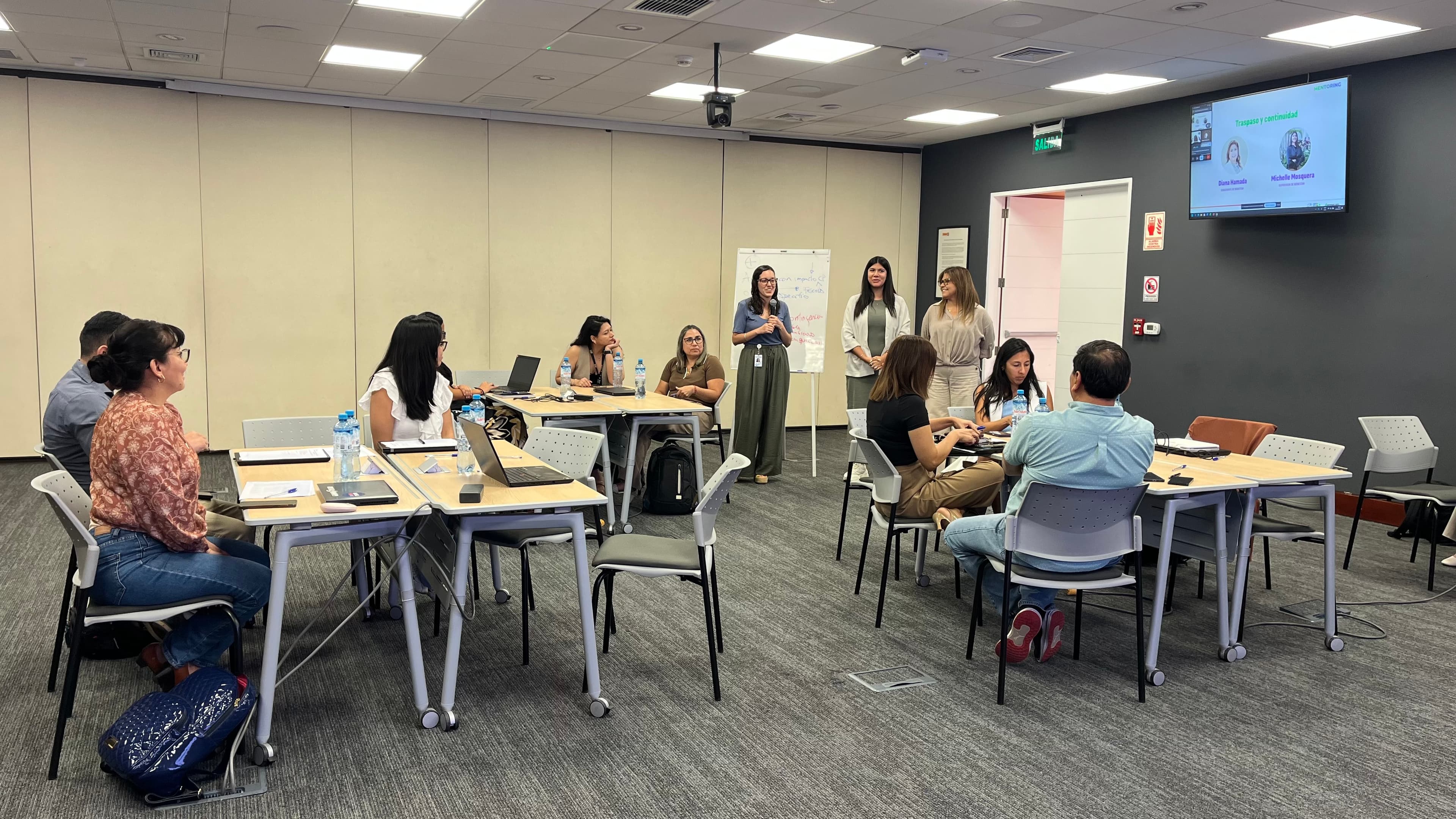 Grupo de profesionales en una capacitación corporativa con una ponente en una sala moderna.